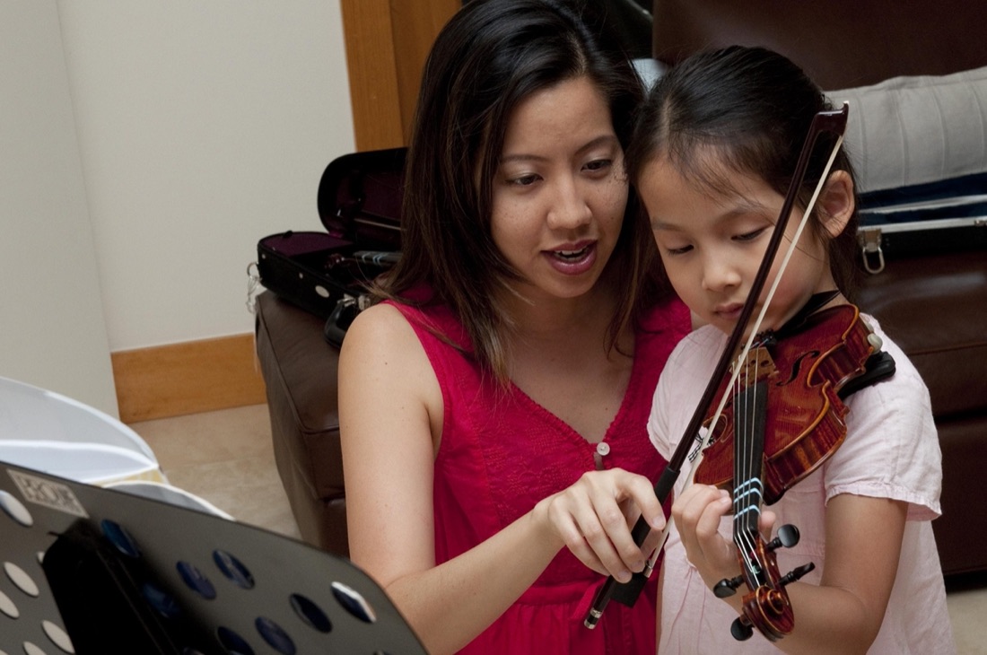 Miss Betty guiding a young student's bow hand
