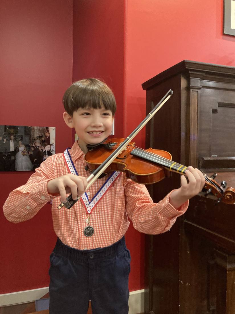 A young violin student smiling after a recital, wearing an award medal